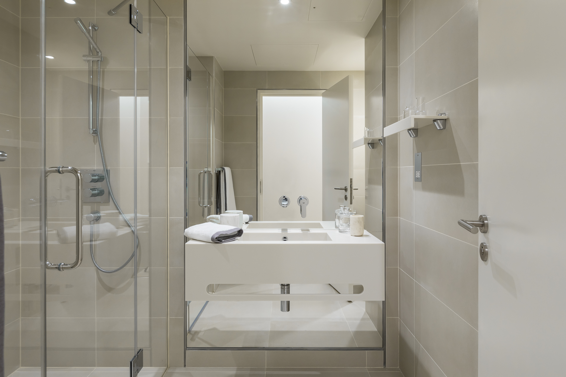 Beige tiled bathroom with sleek and contemporary stainless steel shower accessories and large white counter/basin