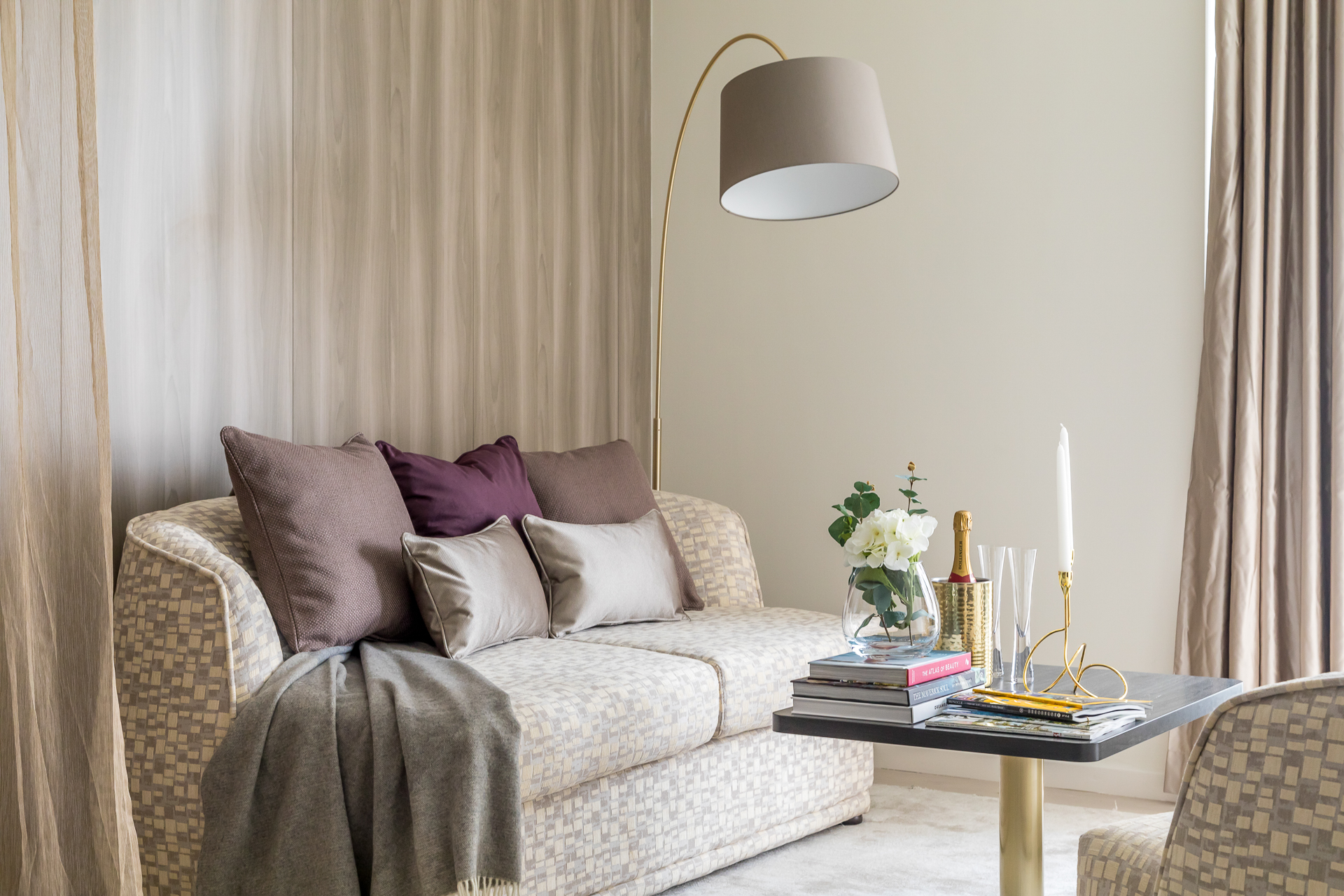 Contemporary, elegant sitting room with patterned sofa and purple and gold details. Luxurious rug carpeting. Wood wall panelling