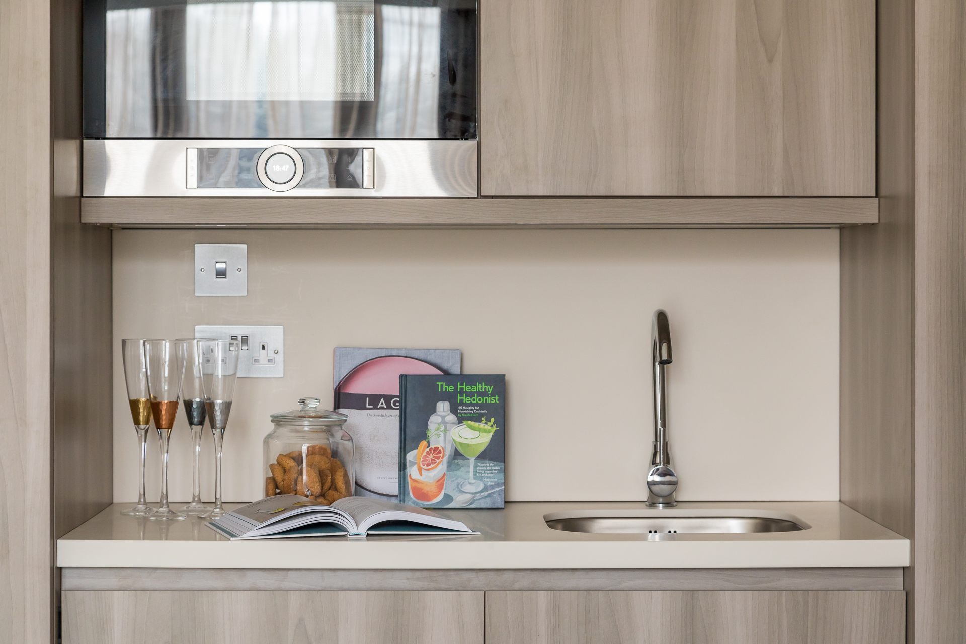 Efficient, minimal kitchen with contemporary appliances, ashy wood doors and white work surfaces. Steel accents