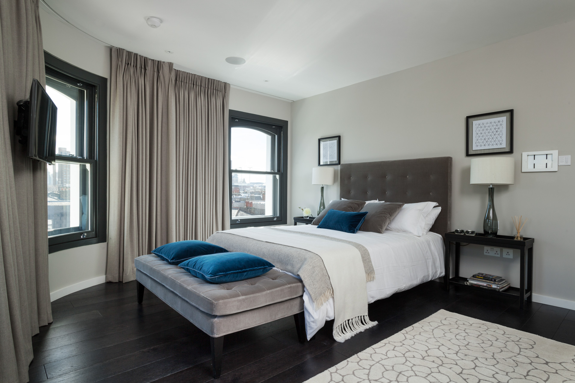 neutral residential master bedroom with high ceilings blue cushions and black stained hardwood floors