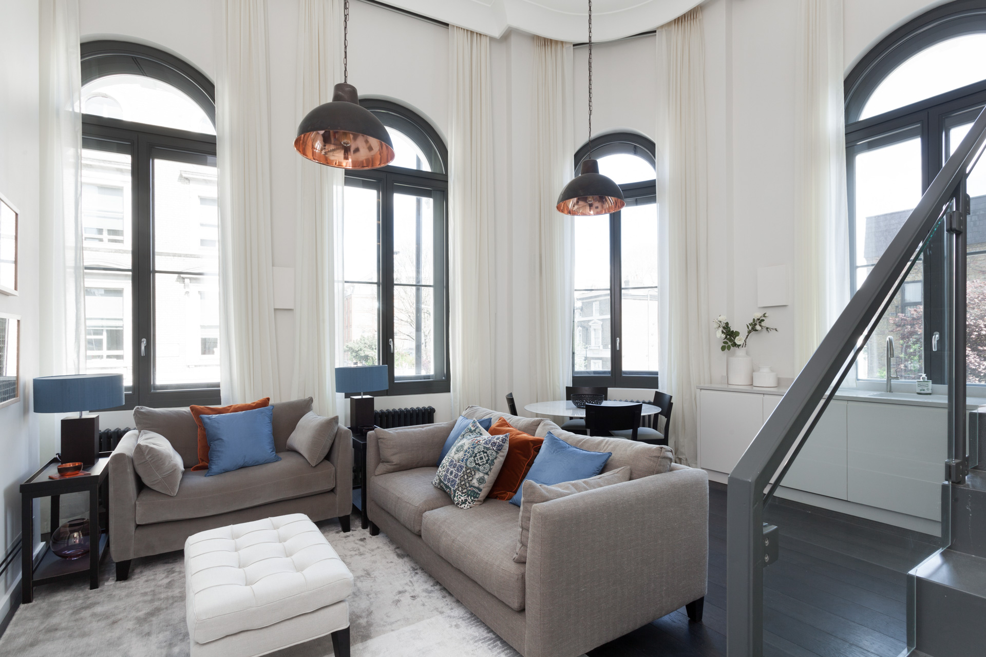 double height living room and dining room with blue, beige and orange with copper accents. Arched window