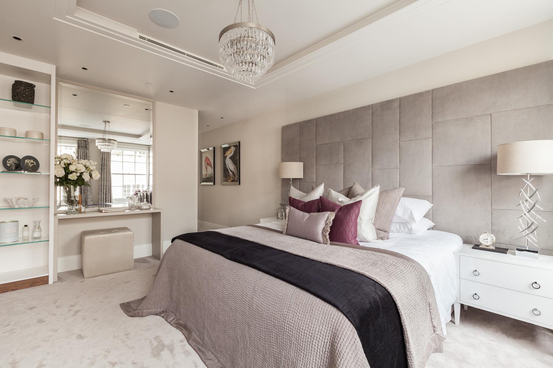 classic glamorous master bedroom with mauve and purple scatter cushions, patterned tufted headboard and glass chandelier