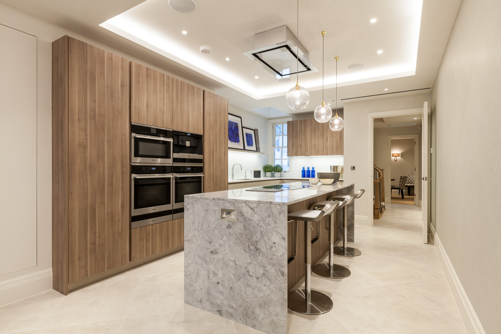 Marble slab counter island in kitchen with recessed ceiling. Neutral scheme of wood with grey and cream